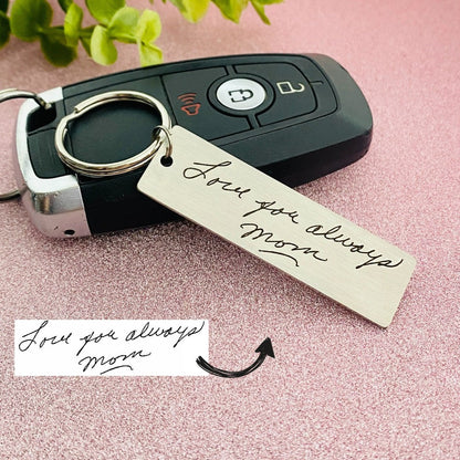 A stainless steel keychain with laser engraved handwriting on it, placed on a car key. 