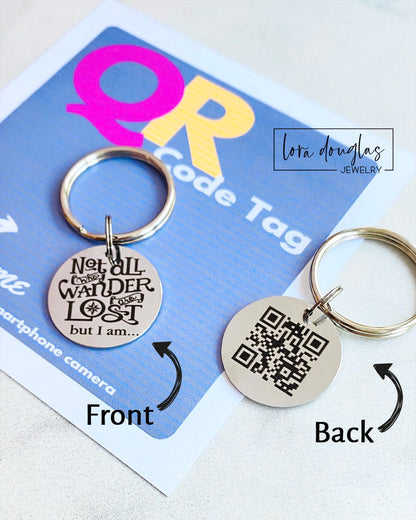A stainless steel QR code pet tag in the shape of a keyring, with the engraved message 'Not all who wander are lost but I am.'.