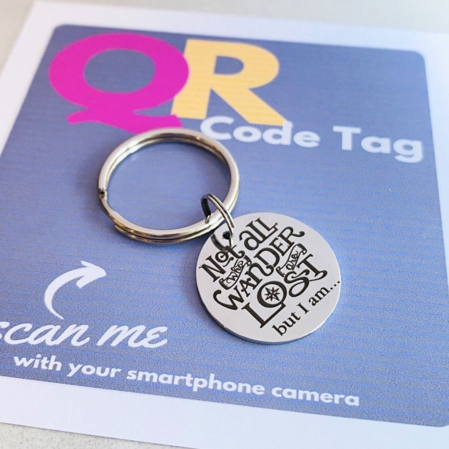 A stainless steel QR code pet tag in the shape of a keyring, with the engraved message 'Not all who wander are lost but I am.'.