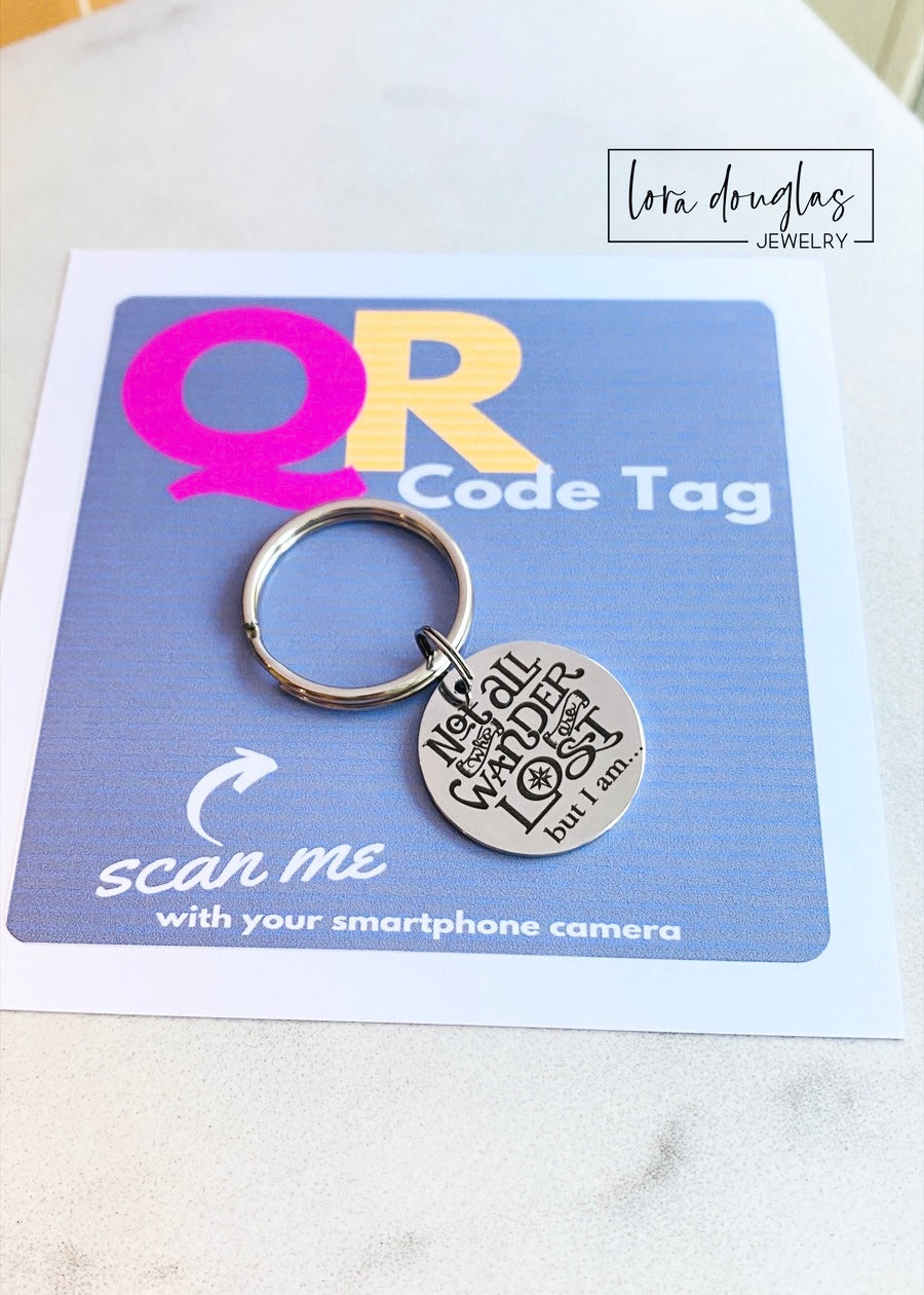 A stainless steel QR code pet tag in the shape of a keyring, with the engraved message 'Not all who wander are lost but I am.'.