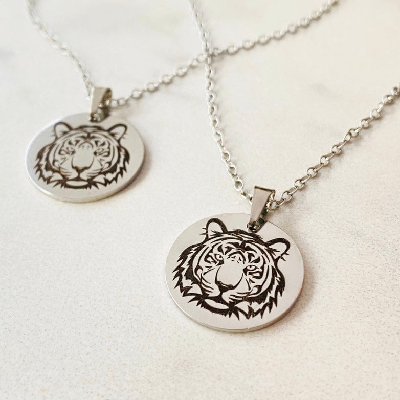 Two pieces of jewelry, a necklace and a bracelet, featuring round pendants with a black and white tiger design on a silver-colored background.