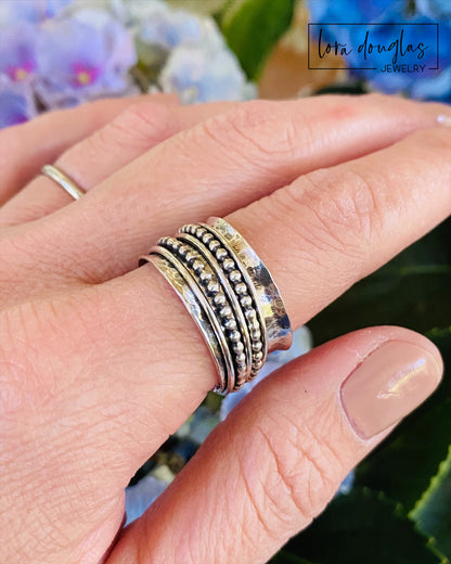 A sterling silver spinner ring with black accents and a textured pattern, presented in a white box