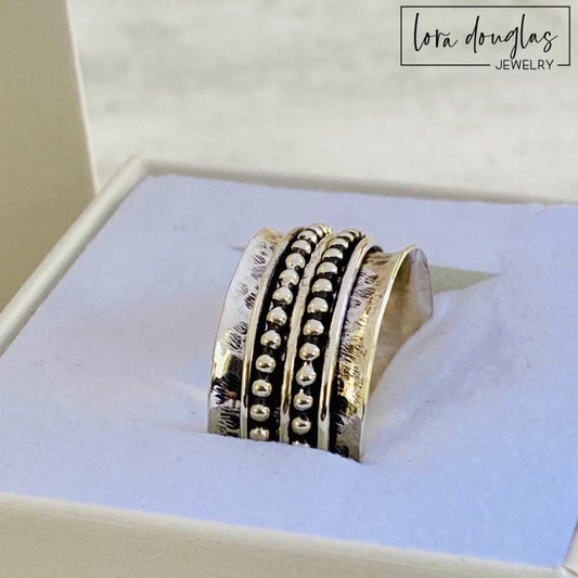 A sterling silver spinner ring with black accents and a textured pattern, presented in a white box