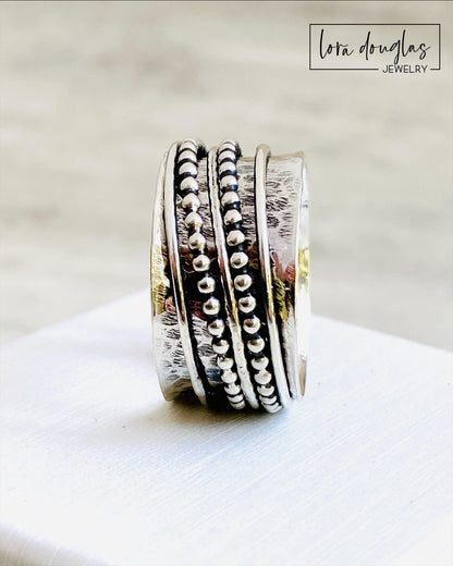 A sterling silver spinner ring with black accents and a textured pattern, presented in a white box