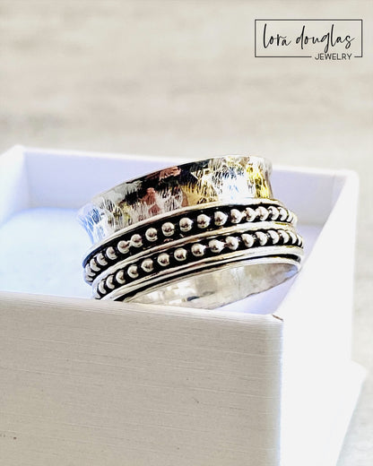 A sterling silver spinner ring with black accents and a textured pattern, presented in a white box
