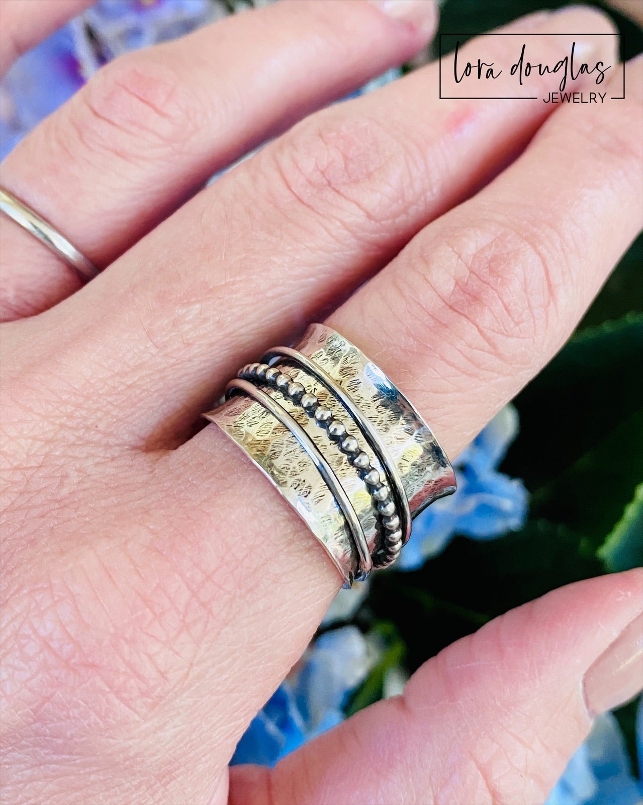 A sterling silver spinner ring with black accents and a textured pattern, presented in a white box