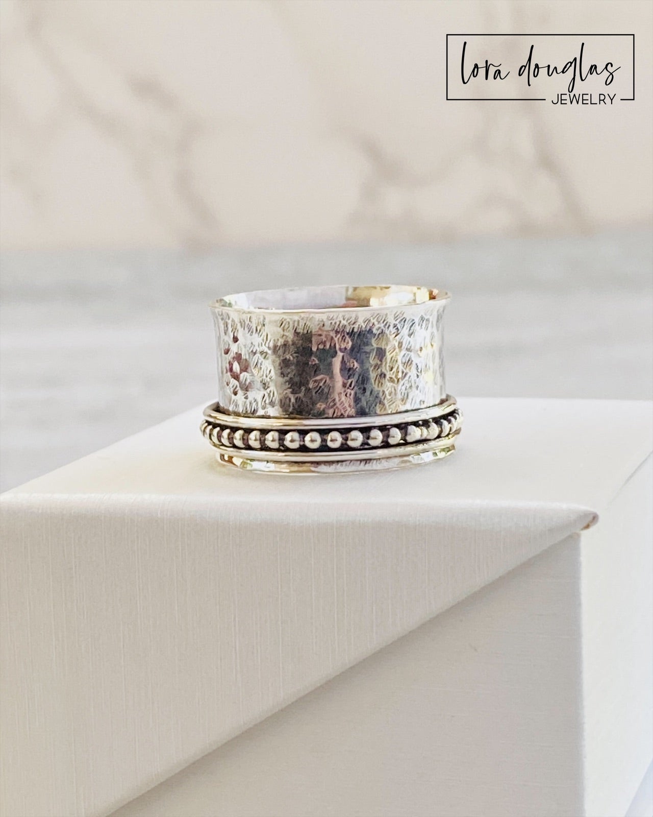 A sterling silver spinner ring with black accents and a textured pattern, presented in a white box