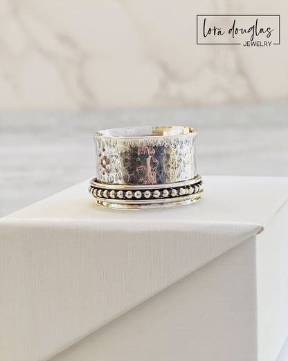 A sterling silver spinner ring with black accents and a textured pattern, presented in a white box