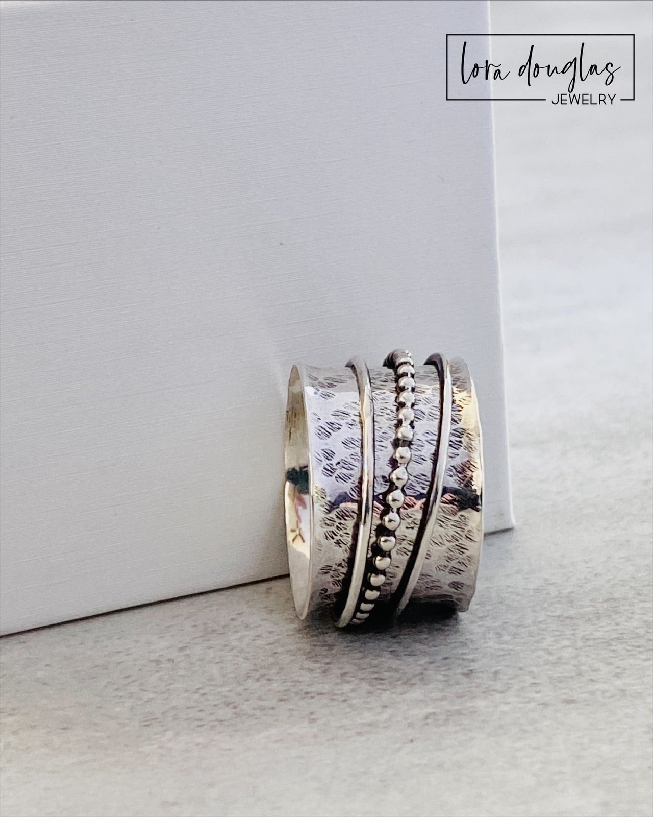 A sterling silver spinner ring with black accents and a textured pattern, presented in a white box