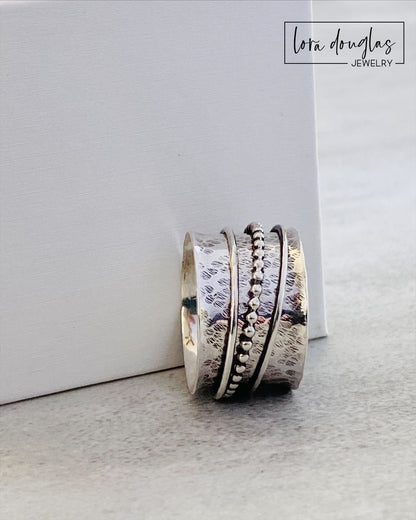 A sterling silver spinner ring with black accents and a textured pattern, presented in a white box