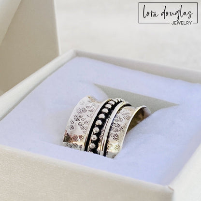 A sterling silver spinner ring with black accents and a textured pattern, presented in a white box