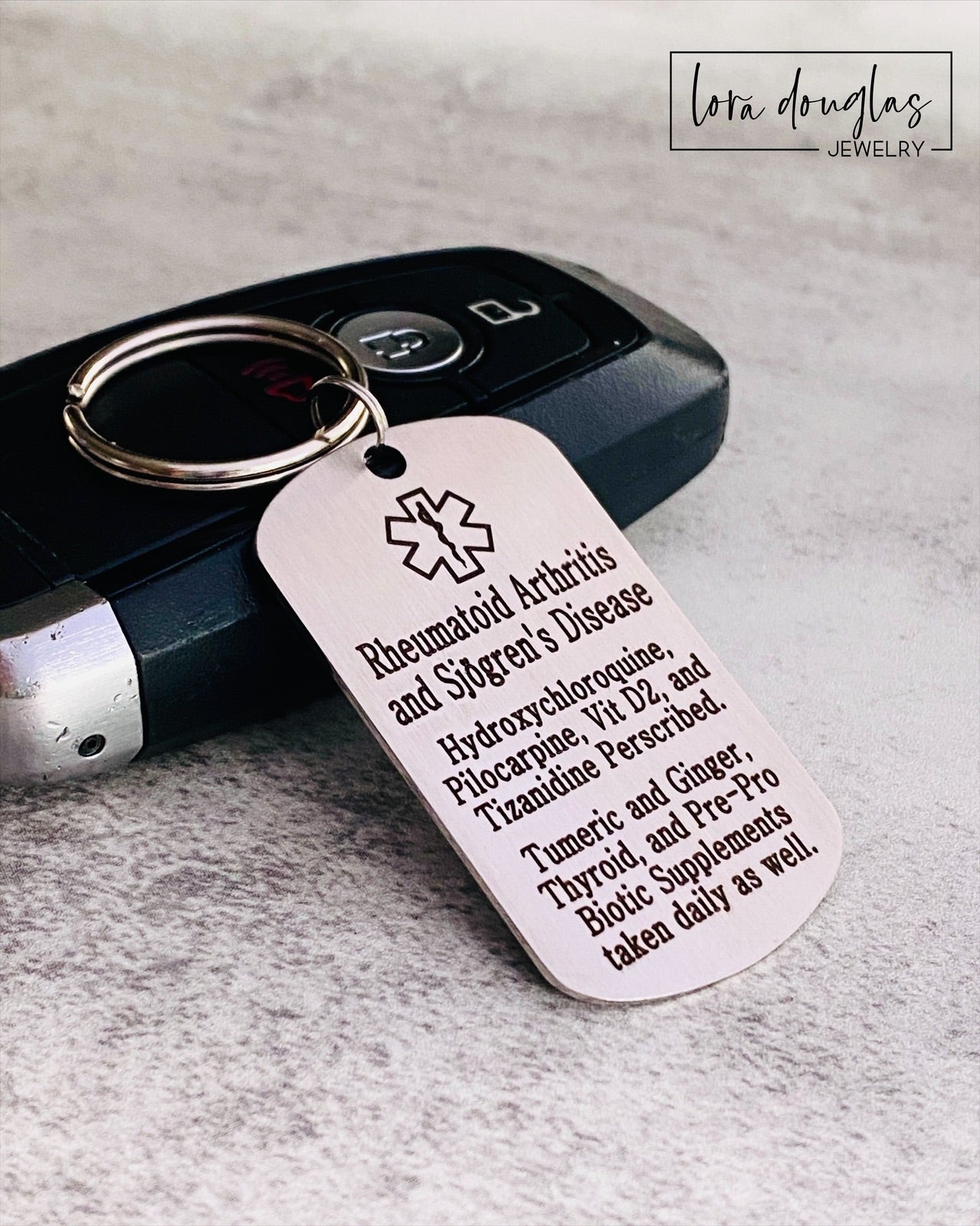 A stainless steel medical alert keychain displayed on a key. The tag has sample text for customization and indicates that additional text can be added on the back.