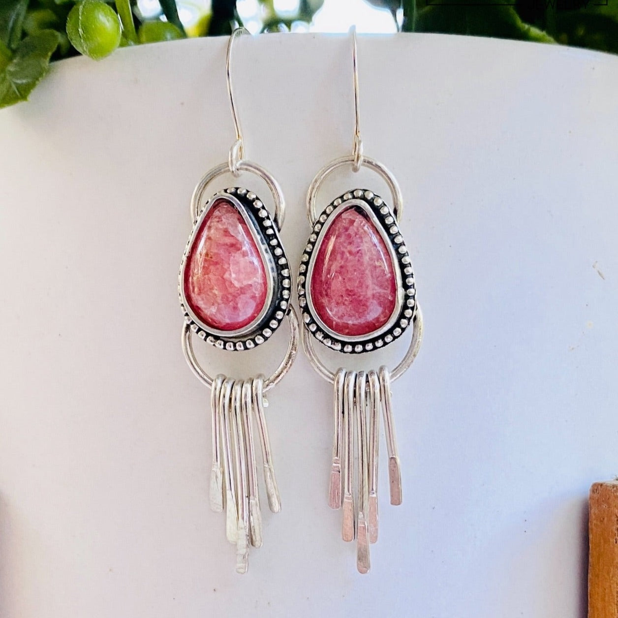 A pair of Rhodochrosite Sterling Silver Fringe Earrings displayed against a white backdrop with green foliage in the background.