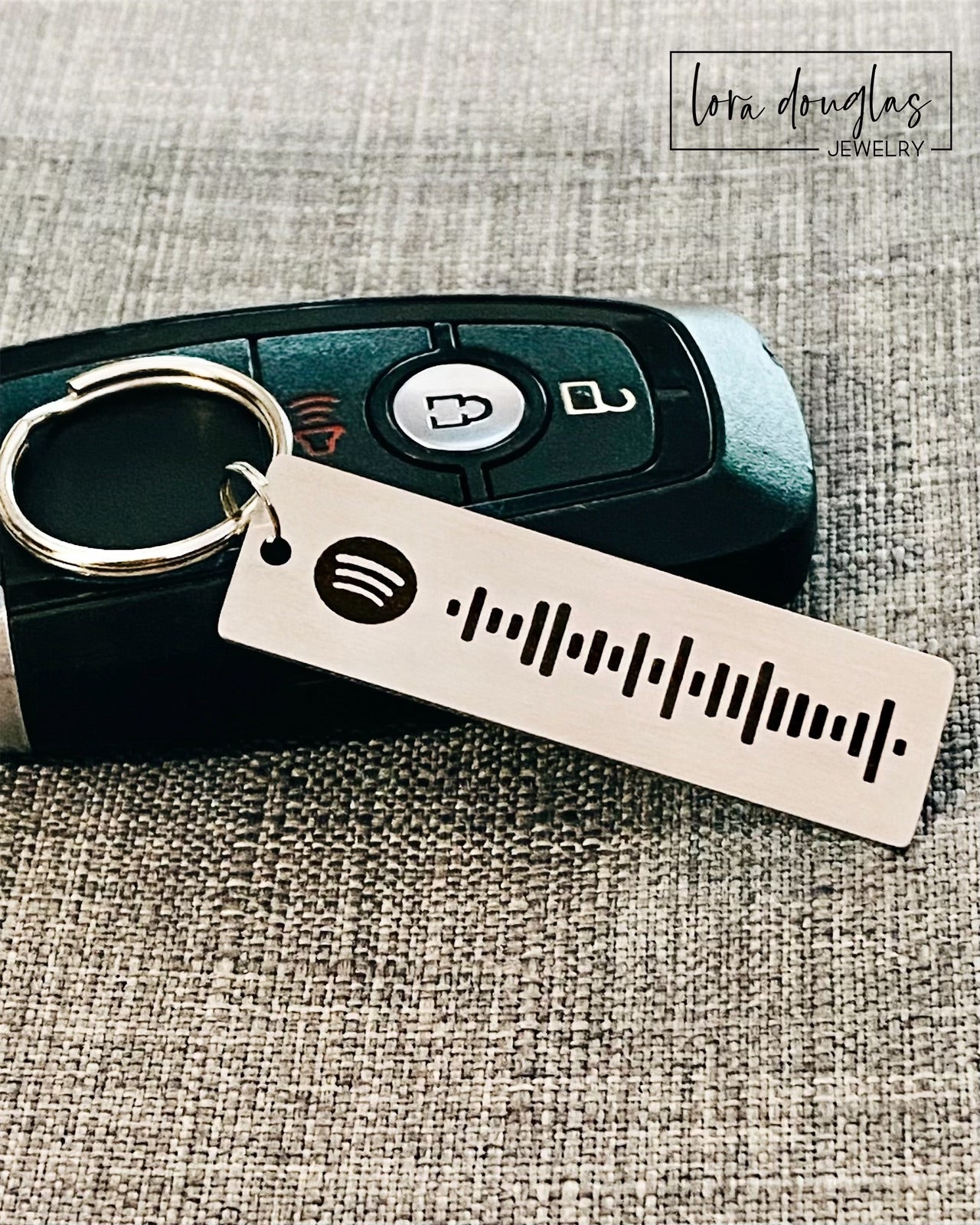 A stainless steel keychain with a laser engraved Spotify code, displayed next to a key fob.