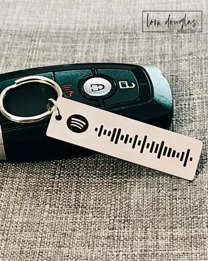 A stainless steel keychain with a laser engraved Spotify code, displayed next to a key fob.