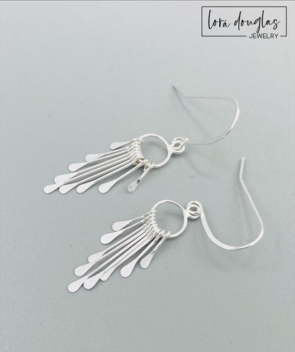 A pair of sterling silver fringe paddle earrings with a drop-style design, featuring small fringes dangling from a main hoop.