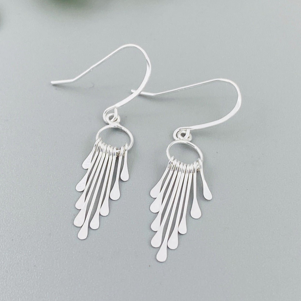 A pair of sterling silver fringe paddle earrings with a drop-style design, featuring small fringes dangling from a main hoop.