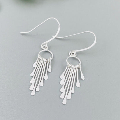 A pair of sterling silver fringe paddle earrings with a drop-style design, featuring small fringes dangling from a main hoop.