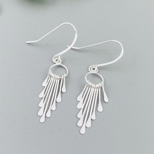 A pair of sterling silver fringe paddle earrings with a drop-style design, featuring small fringes dangling from a main hoop.