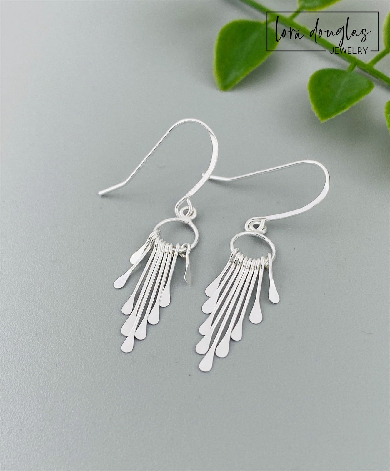 A pair of sterling silver fringe paddle earrings with a drop-style design, featuring small fringes dangling from a main hoop.