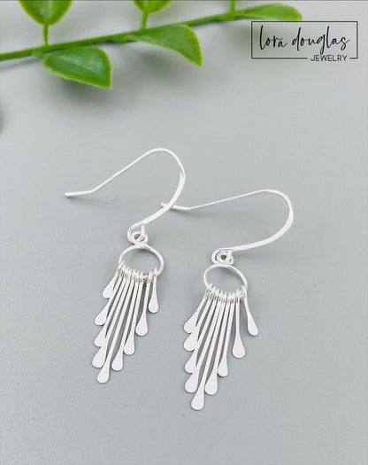 A pair of sterling silver fringe paddle earrings with a drop-style design, featuring small fringes dangling from a main hoop.