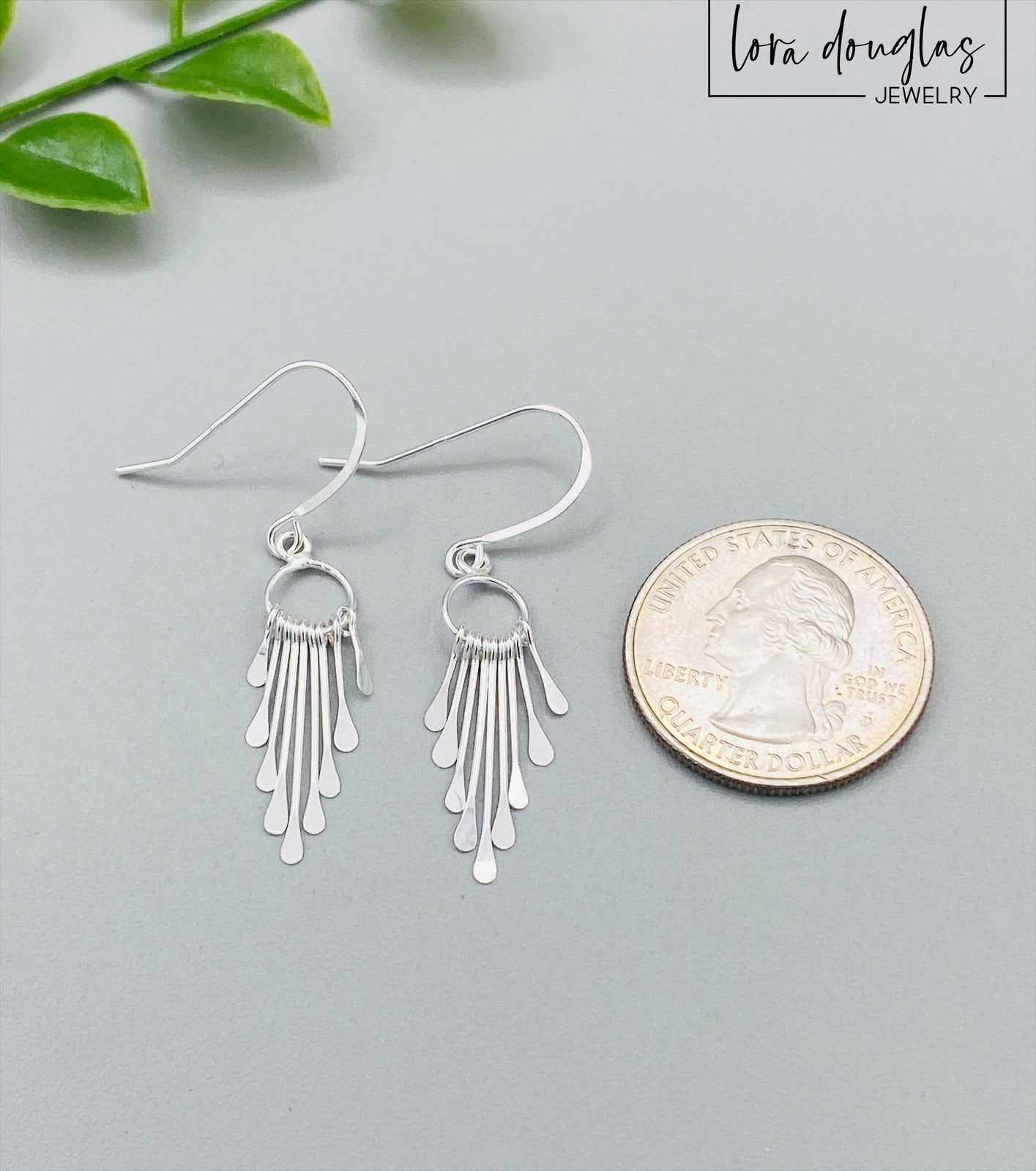 A pair of sterling silver fringe paddle earrings with a drop-style design, featuring small fringes dangling from a main hoop.