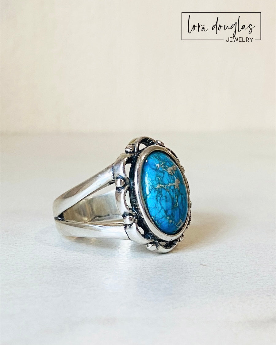 A sterling silver ring with a blue sea sediment jasper gemstone, placed on a white surface.