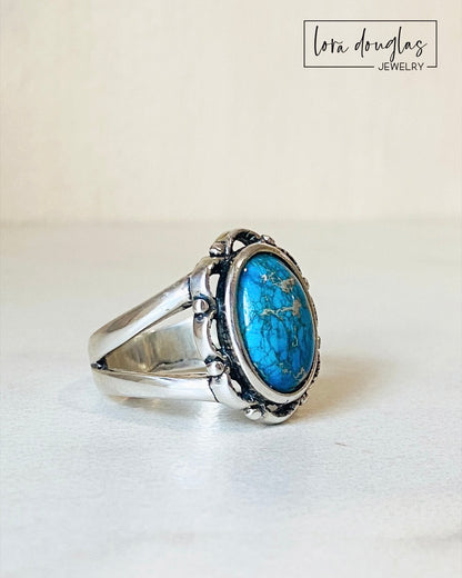 A sterling silver ring with a blue sea sediment jasper gemstone, placed on a white surface.