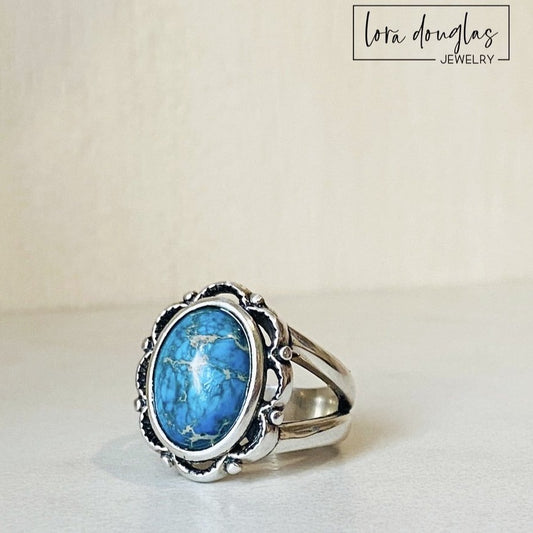 A sterling silver ring with a blue sea sediment jasper gemstone, placed on a white surface.
