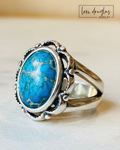 A sterling silver ring with a blue sea sediment jasper gemstone, placed on a white surface.