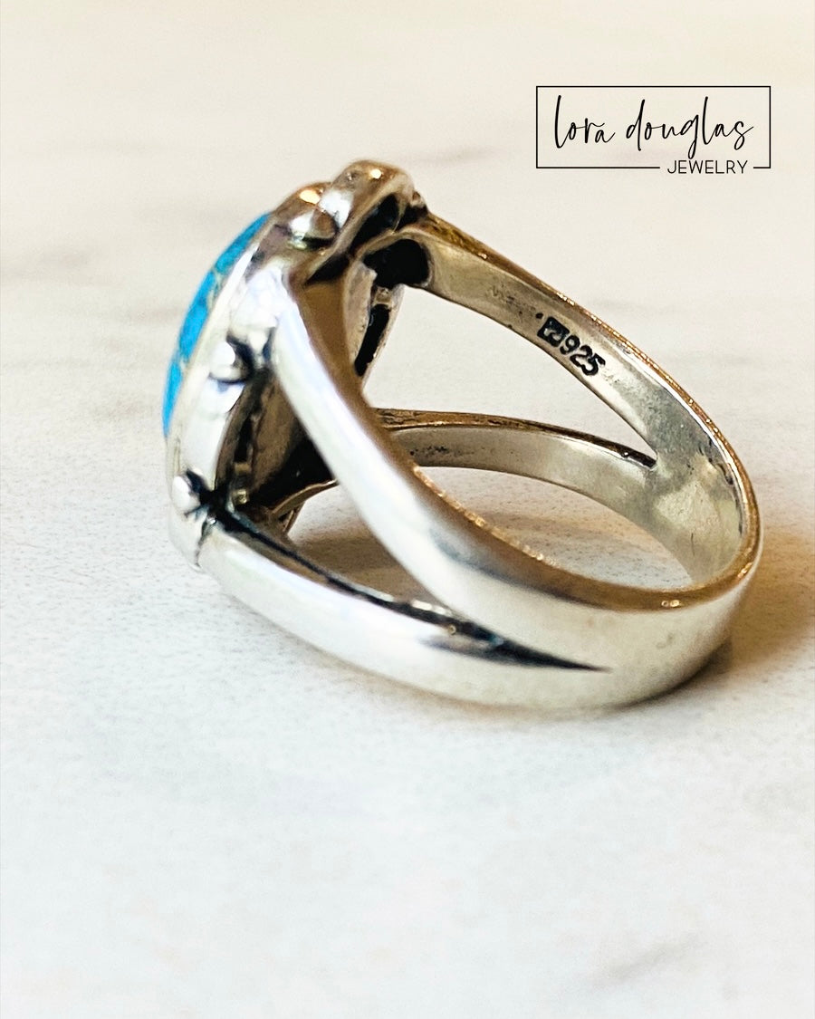 A sterling silver ring with a blue sea sediment jasper gemstone, placed on a white surface.