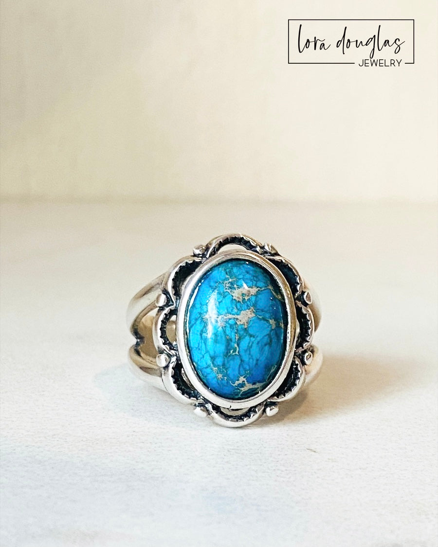 A sterling silver ring with a blue sea sediment jasper gemstone, placed on a white surface.