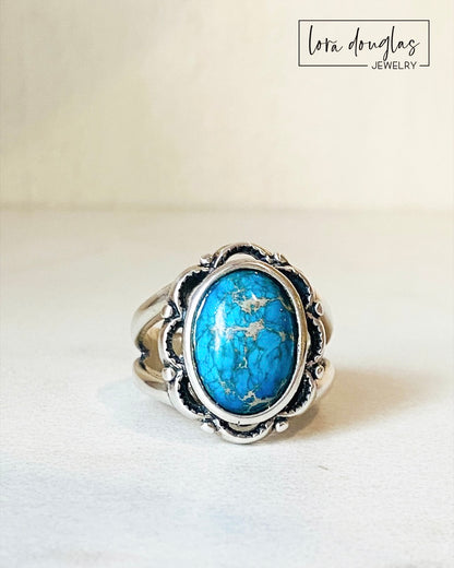 A sterling silver ring with a blue sea sediment jasper gemstone, placed on a white surface.