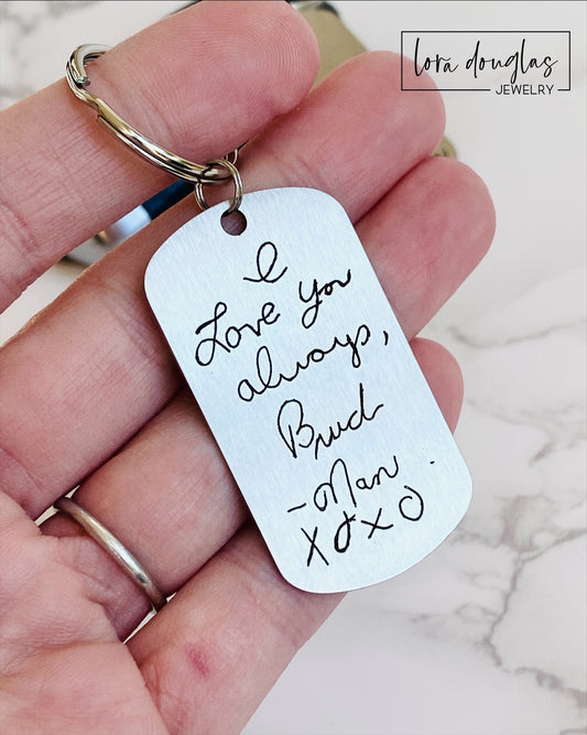 Two silver stainless steel keychains with engraved handwritten messages attached to a keyring, displayed alongside a close-up of the engraved text and an instruction image for capturing suitable images for engraving.