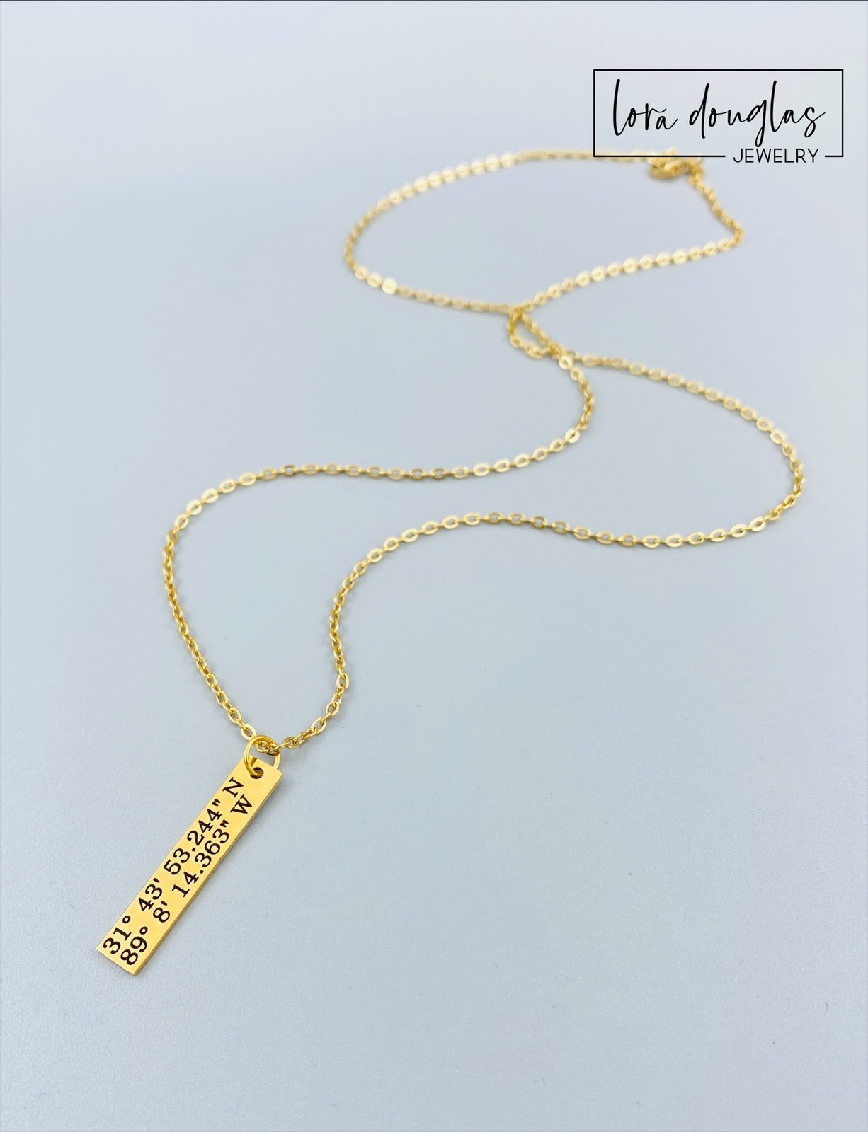 gold necklace engraved with latitude and longitude coordinates in a box that says where it all began