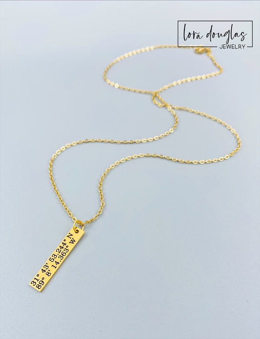 gold necklace engraved with latitude and longitude coordinates in a box that says where it all began
