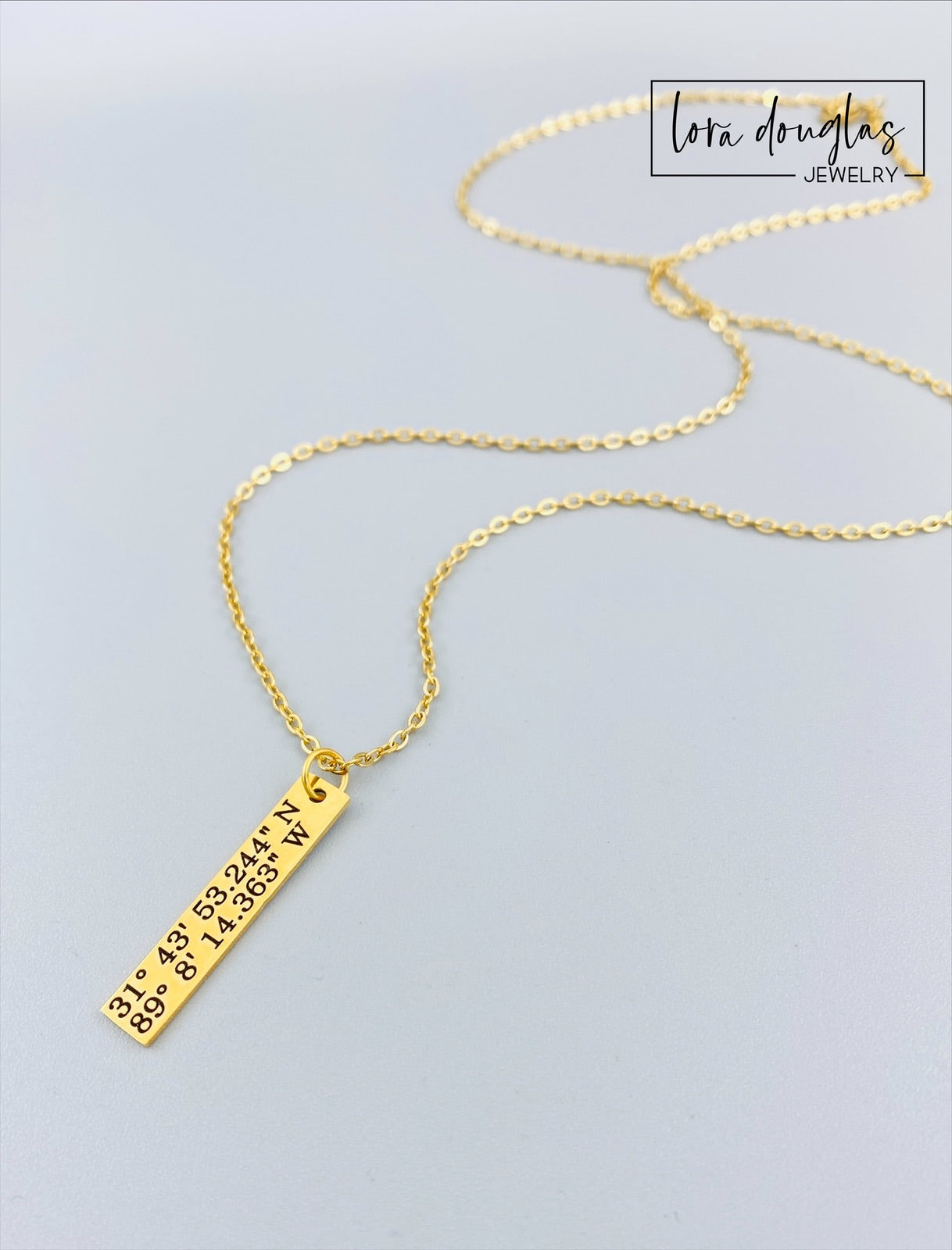 gold necklace engraved with latitude and longitude coordinates in a box that says where it all began