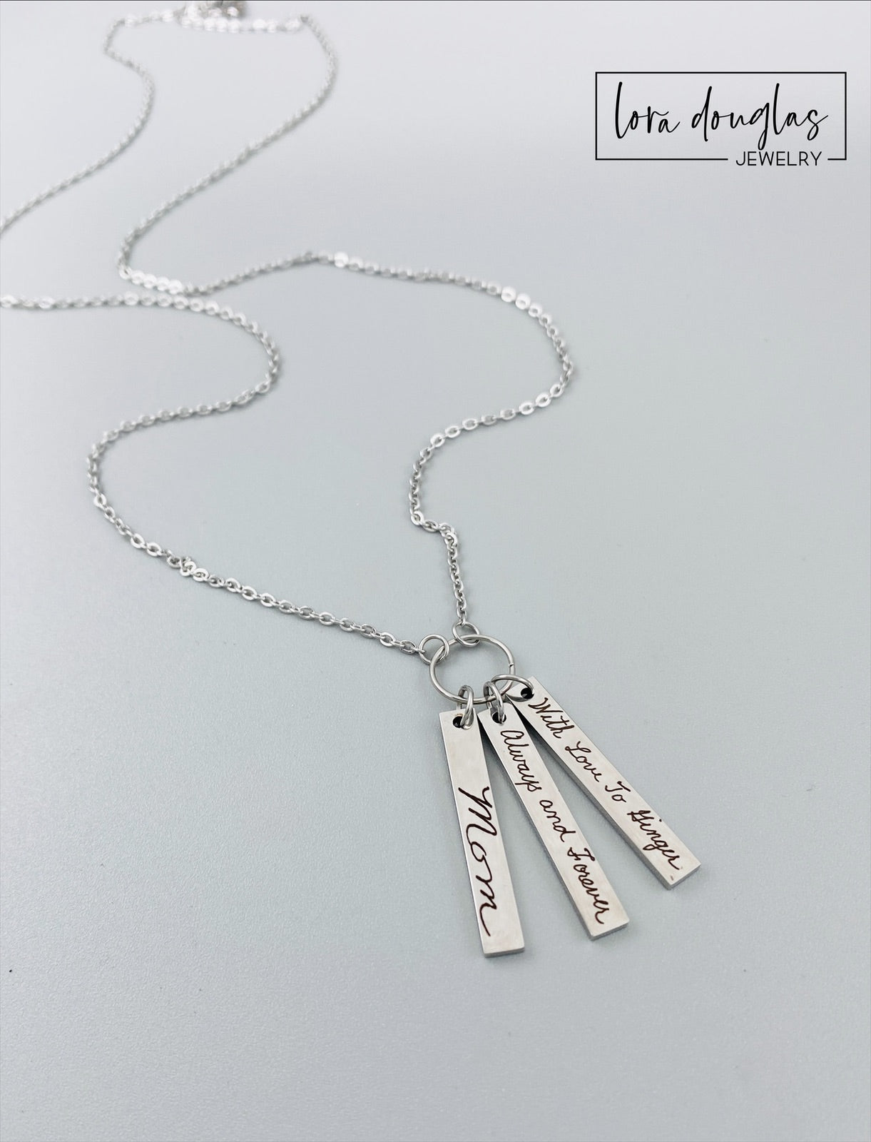 A silver stainless steel necklace with a chain and three rectangular pendants, each engraved with different handwriting.