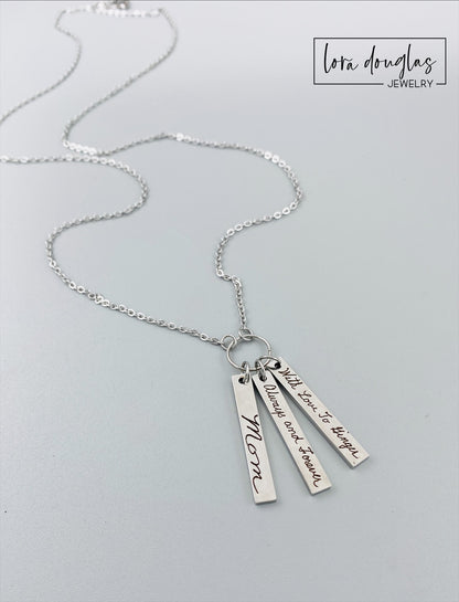 A silver stainless steel necklace with a chain and three rectangular pendants, each engraved with different handwriting.