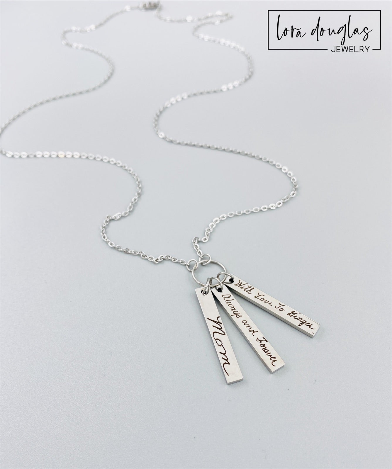 A silver stainless steel necklace with a chain and three rectangular pendants, each engraved with different handwriting.