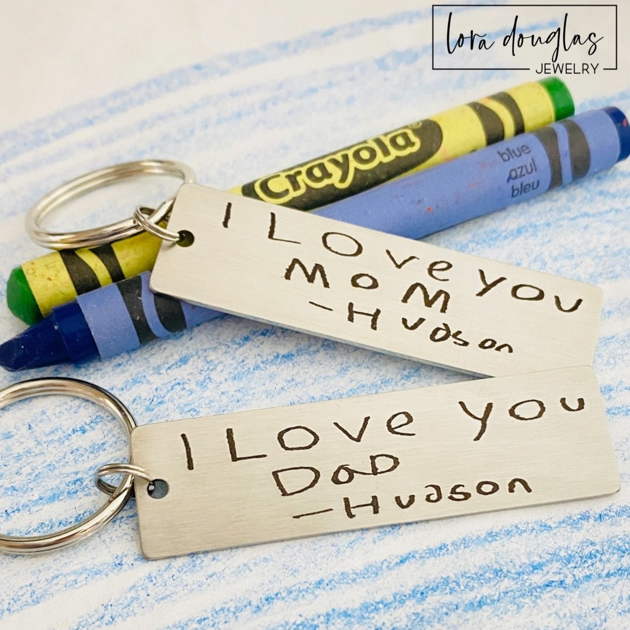 A stainless steel keychain with engraved handwriting samples. The keychain features a silver-colored plate with the text 'I love you dad' and 'Mom you're the best' alongside a standard key ring.