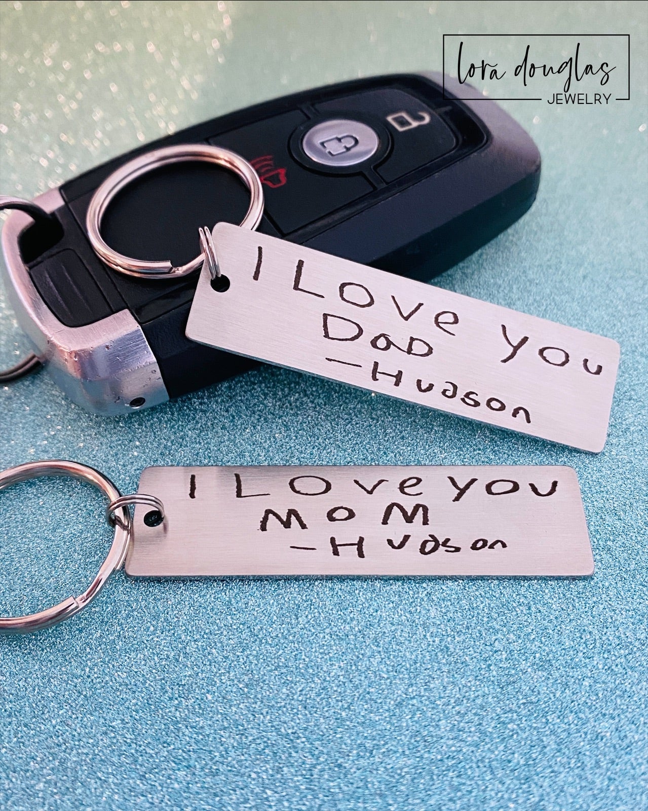 A stainless steel keychain with engraved handwriting samples. The keychain features a silver-colored plate with the text 'I love you dad' and 'Mom you're the best' alongside a standard key ring.