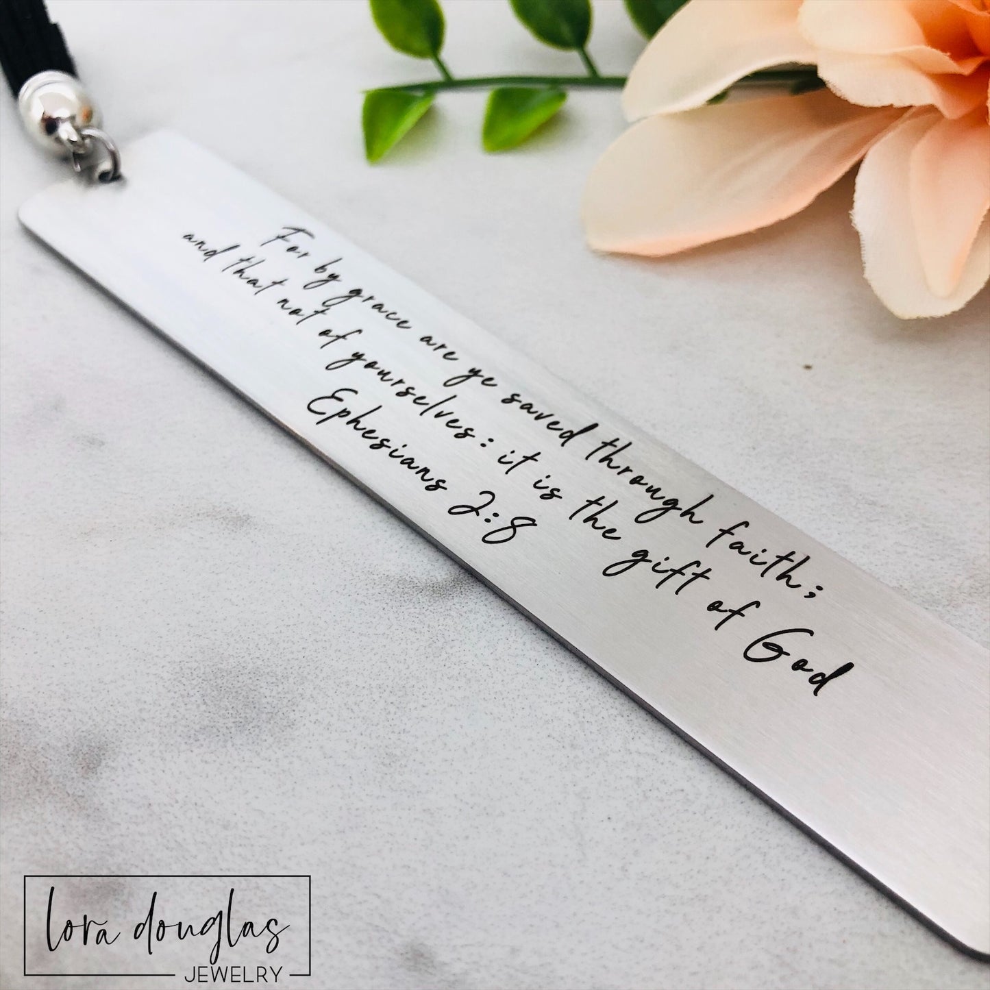 engraved christian bookmark with custom Bible verse shown close up on stainless steel surface, personalized scripture bookmark with tassel designed for Bible study gifts and faith based readers