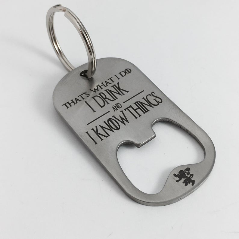 A stainless steel key chain with the engraved text 'That's What I Do I Drink and I Know Things' along with the HBO logo for Game of Thrones, resting on a corkscrew.