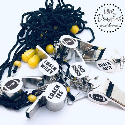 personalized stainless steel whistles with engraved text, one with 'COACH CARLOS' and sports icons, the other with 'FOOTBALL BASKETBALL SOCCER LIFEGUARD AND MORE'. Both whistles have a lanyard 