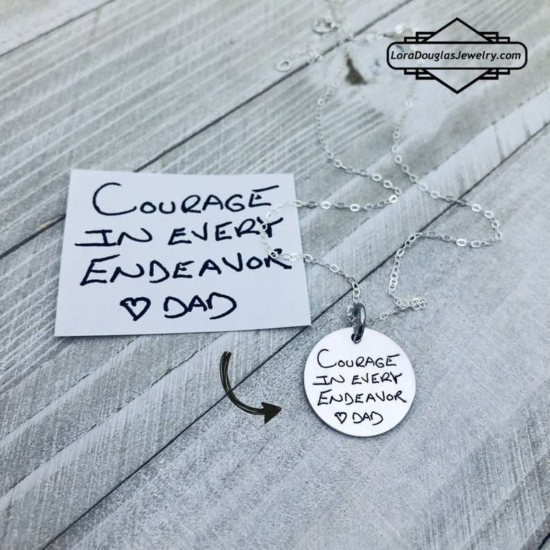 A round silver pendant with engraved with handwritten text 