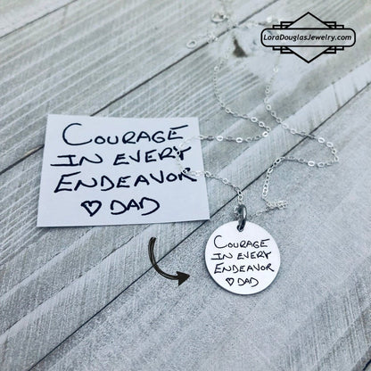 A round silver pendant with engraved with handwritten text 