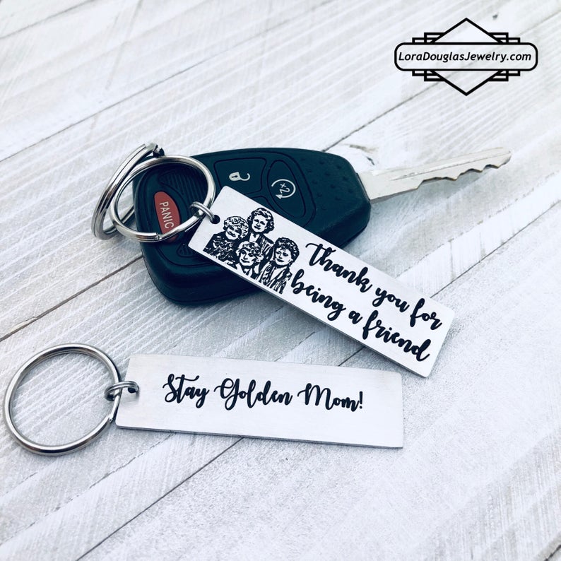 A stainless steel key chain with an engraved design of the Golden Girls characters and the text 'Thank you for being a friend'.