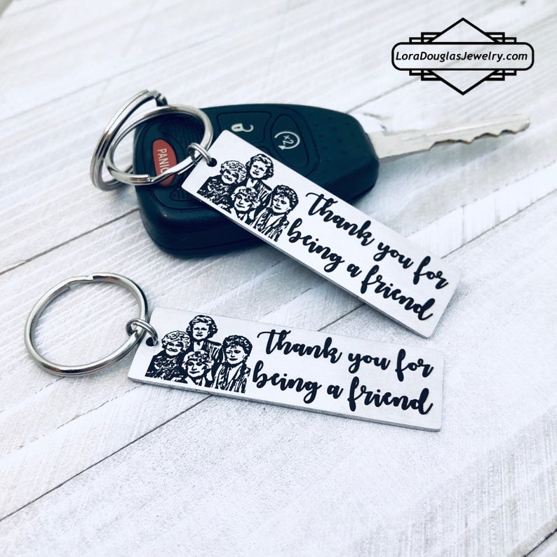 A stainless steel key chain with an engraved design of the Golden Girls characters and the text 'Thank you for being a friend'.