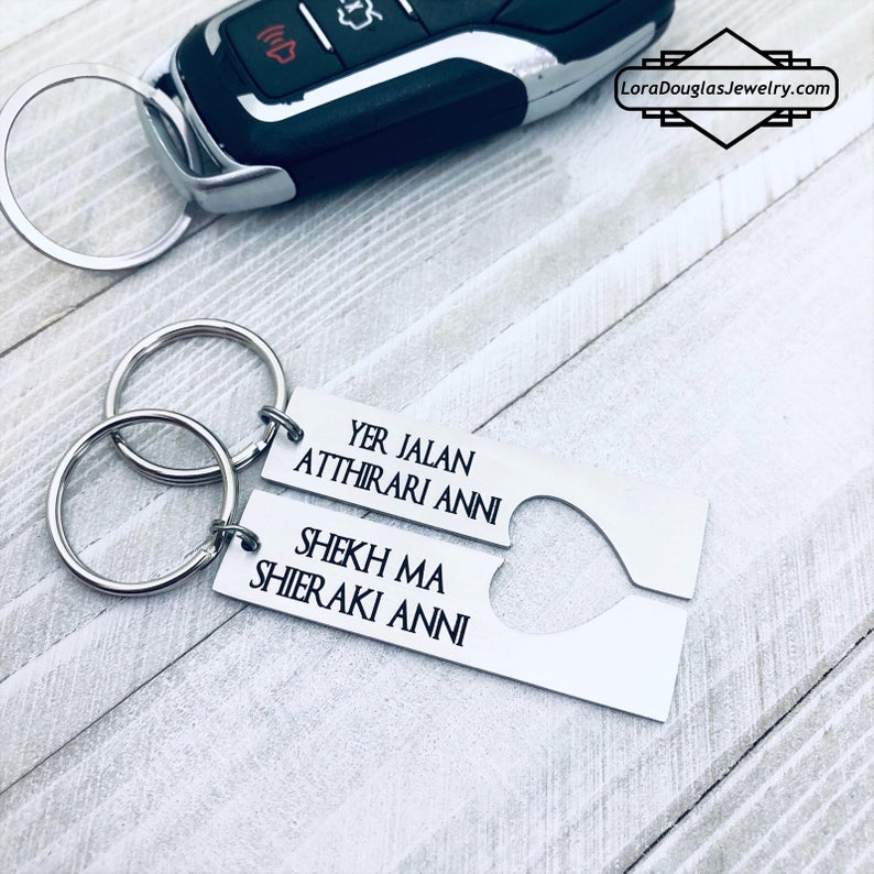 Two silver stainless steel keychains with Dothraki engraving, presented on a car key. One keychain reads 'Yer Jalan Atthirari Anni' and the other reads 'Shekh Ma Shieraki Anni', with optional personalization. Game of Thrones Gift